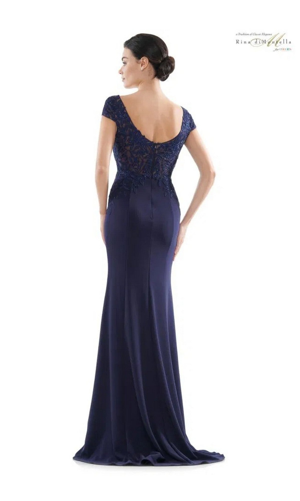 A woman models the Long Formal Dress: Rina Di Montella RD2718—a fitted, floor-length navy gown with an embroidered bodice and cap sleeves—shown from the back against a plain white background.